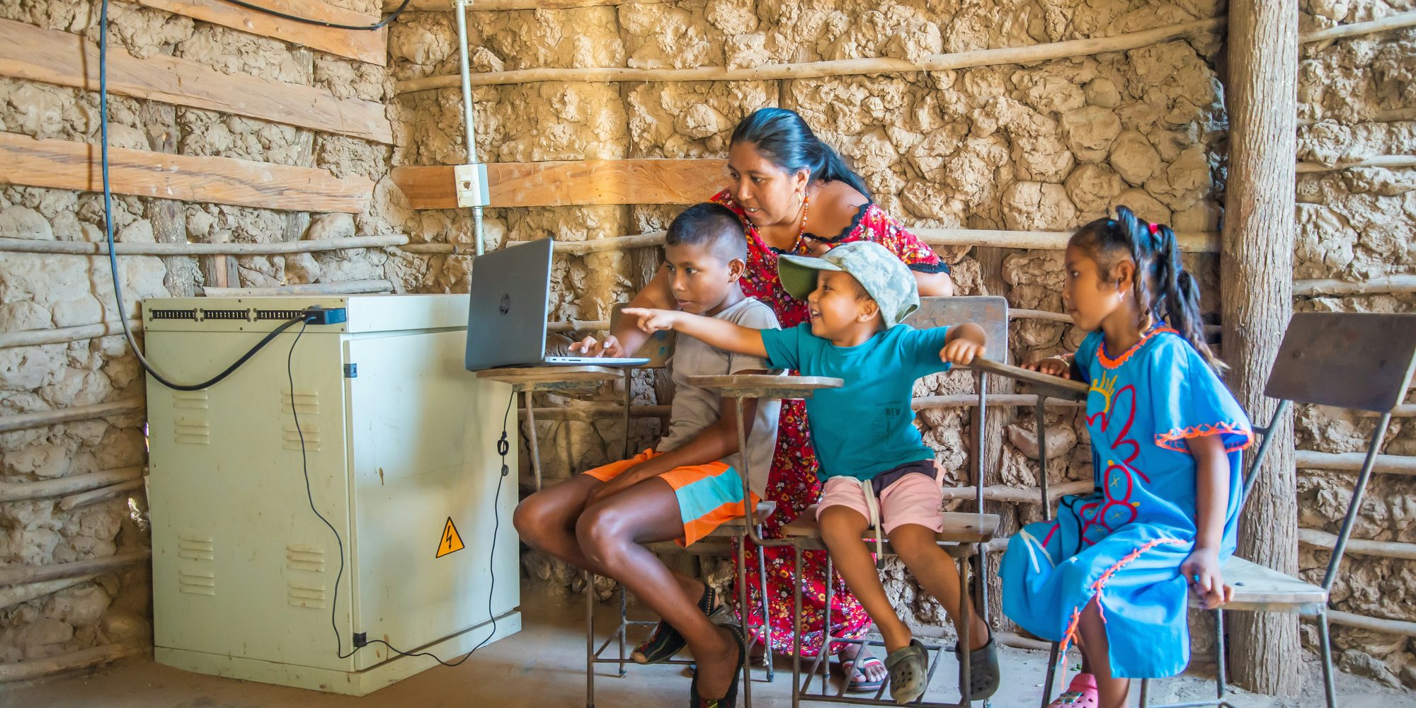 A teacher helping children learn on a laptop in a rural classroom